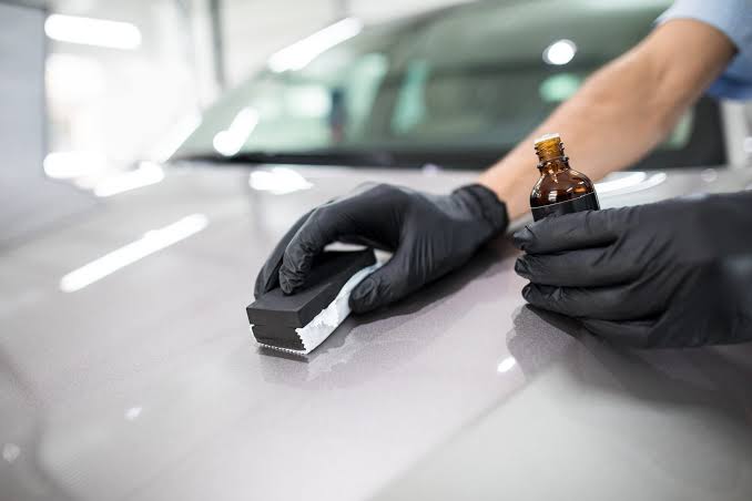 Close-up of a technician expertly applying ceramic coating to a car's surface, highlighting the resulting deep gloss and protective layer